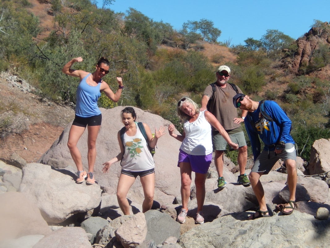 Five hikers resting on massive boulders above a dark canyon pool near Loreto