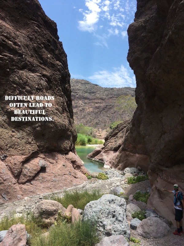 Hikers on a boulder-strewn canyon trail with a motivational quote overlay, Loreto 2017