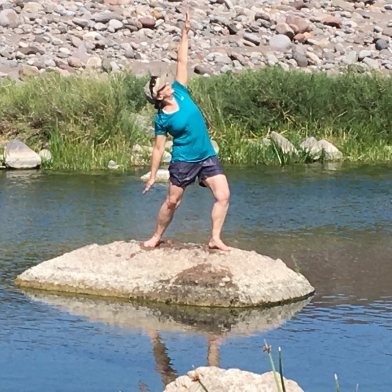 Person stretching on a rock beside a clear river in a Baja canyon