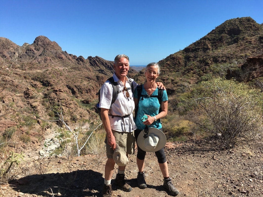Two hikers on a trail with rugged desert mountains rising behind them near Loreto