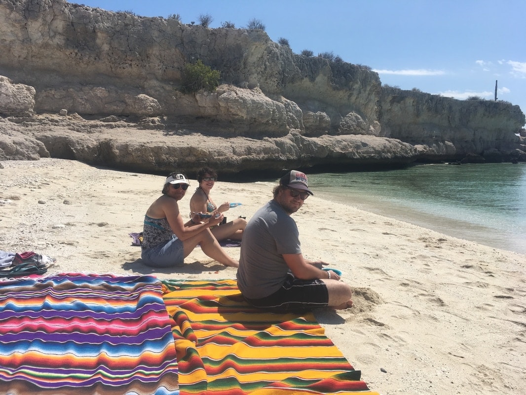 Guests relaxing on colorful Mexican blankets on a white sand beach cove on a Loreto island tour