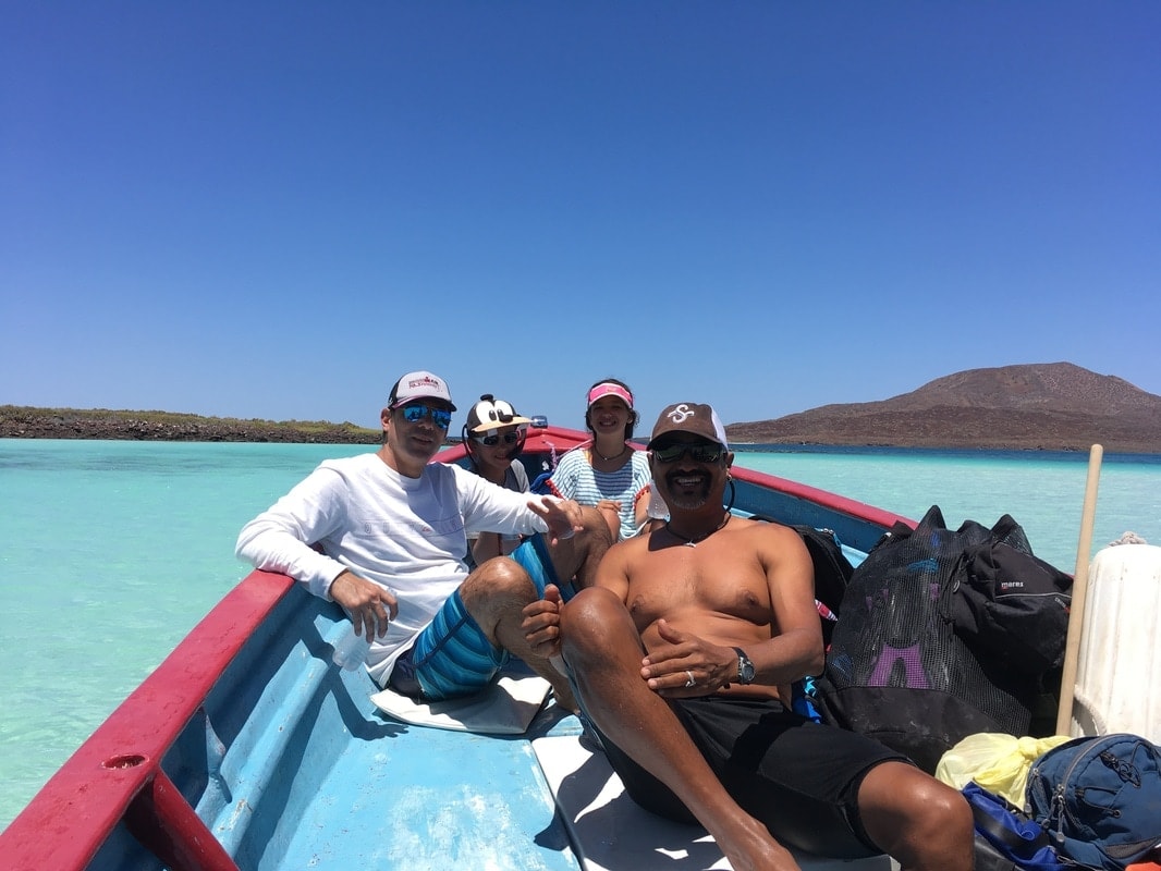 Four people relaxing on a traditional panga boat in brilliant turquoise water near a Loreto island