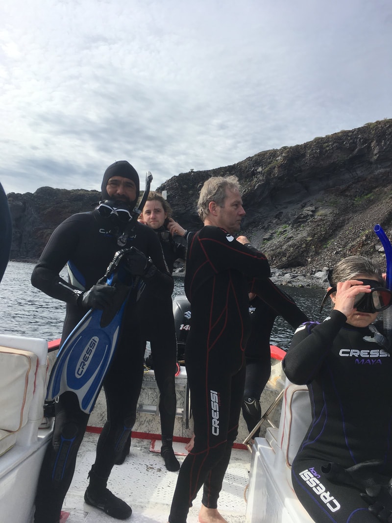 Four people in Cressi wetsuits gearing up with fins and masks on a boat with dark volcanic cliffs rising behind them on a Loreto snorkeling tour