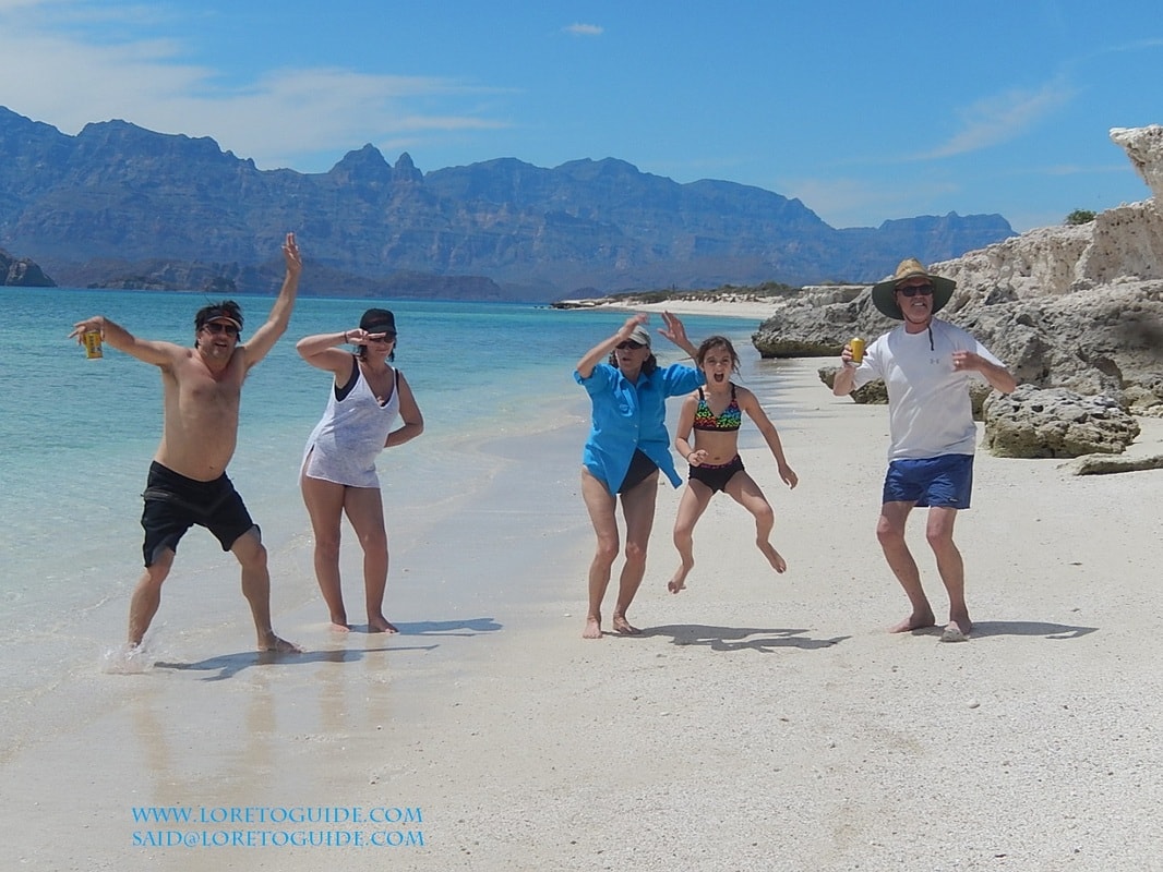 Family of five jumping and celebrating on a white sand beach with turquoise water and sierra mountains on a Loreto island tour