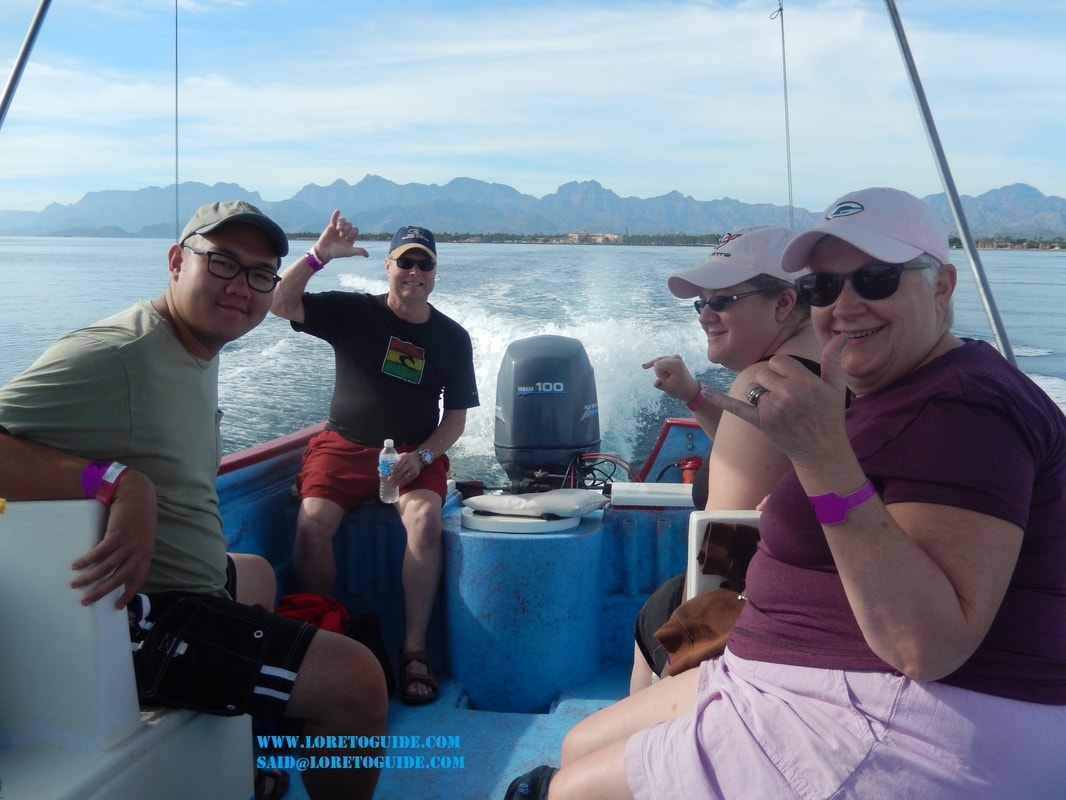 Four happy guests on a panga boat with the Sierra de la Giganta mountains behind them on a Loreto island tour