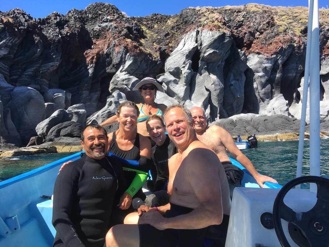 Guide and four happy guests laughing together on a blue panga with towering volcanic rock walls behind them on a Loreto island tour