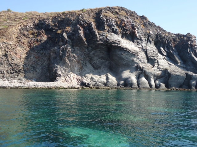 Layered dark volcanic rock cliff meeting crystal-clear turquoise water on a Loreto island tour