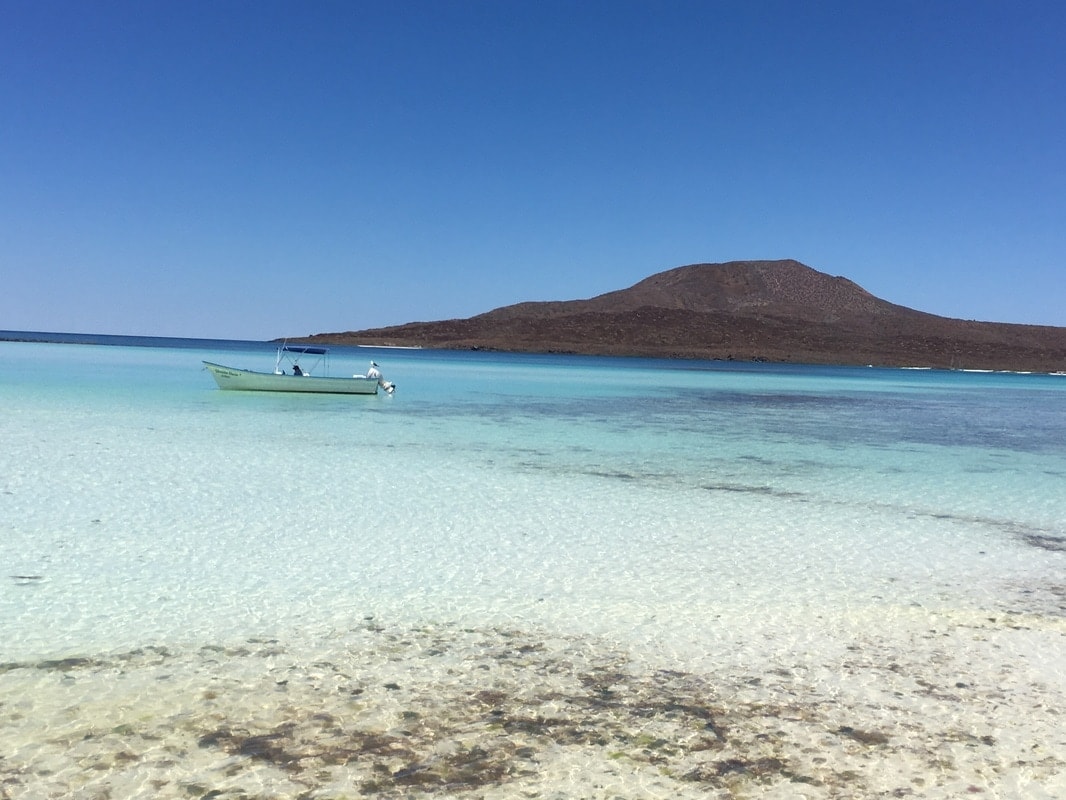 Panga anchored in a glassy crystal-clear lagoon with a perfectly shaped volcanic island rising in the background near Loreto