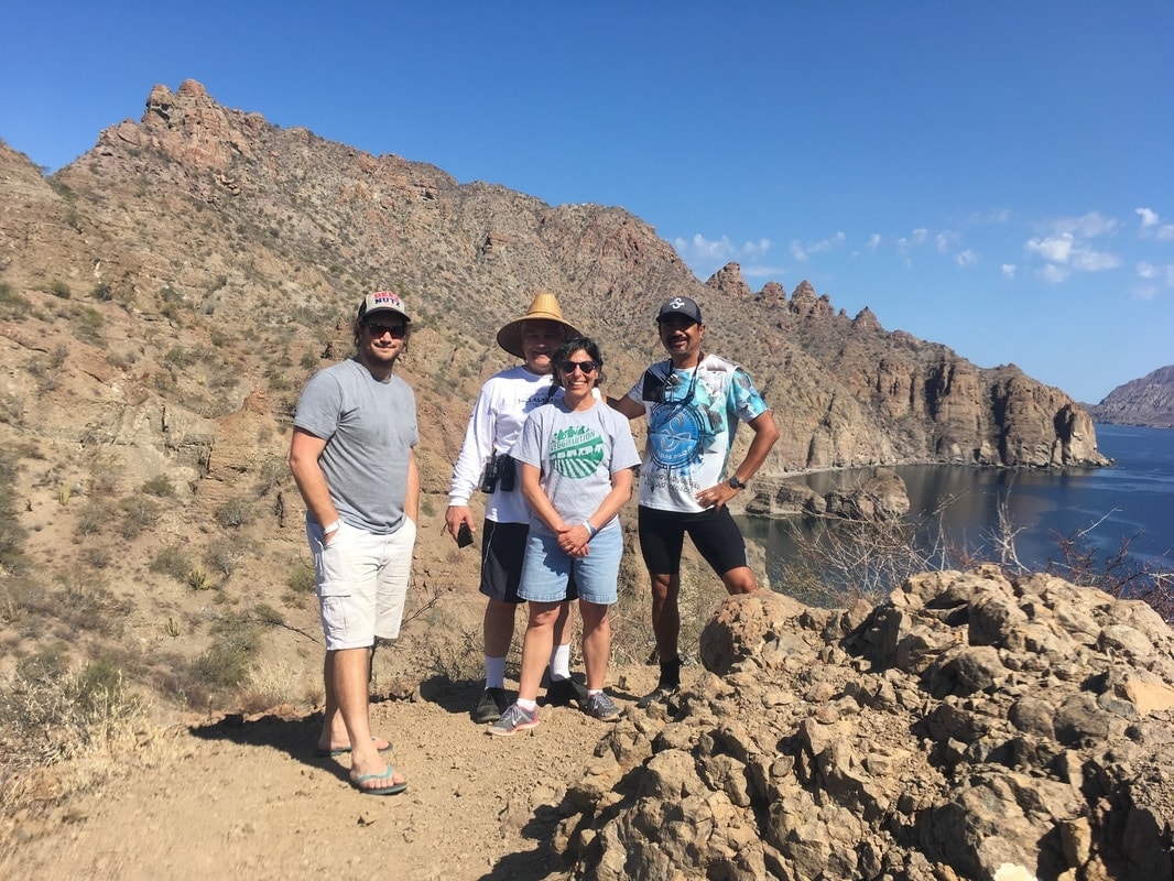 Four people posing on a rocky coastal ridge with dramatic gulf and mountain views on a Loreto island tour