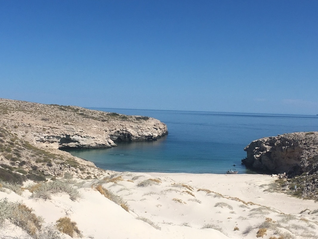 Secluded white sand cove perfectly framed by pale limestone cliffs with a lone panga anchored in turquoise water near Loreto