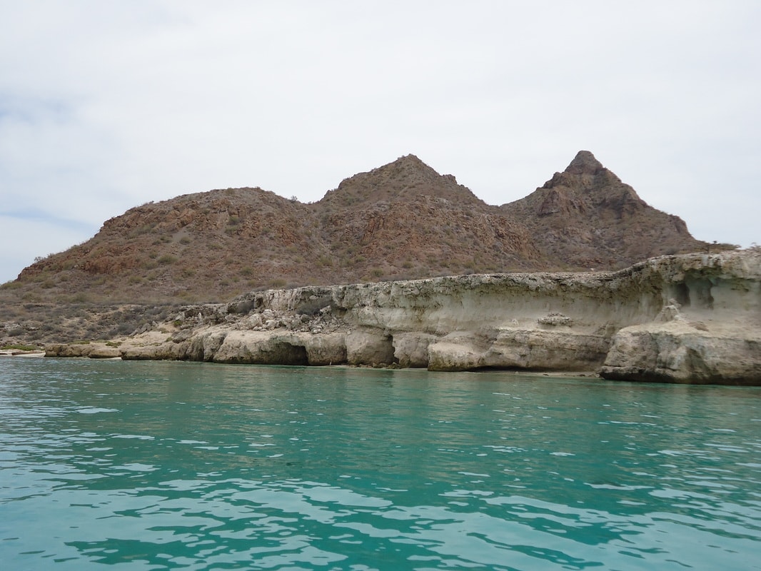 Turquoise waters lapping against white limestone cliffs with twin mountain peaks on a Loreto island tour